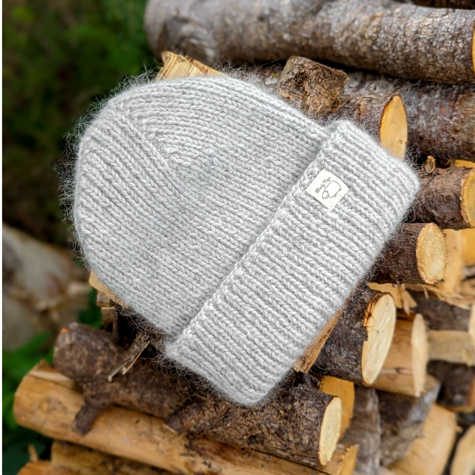 Hand-knitted Wooly Top hat in grey sitting on a pile of logs.