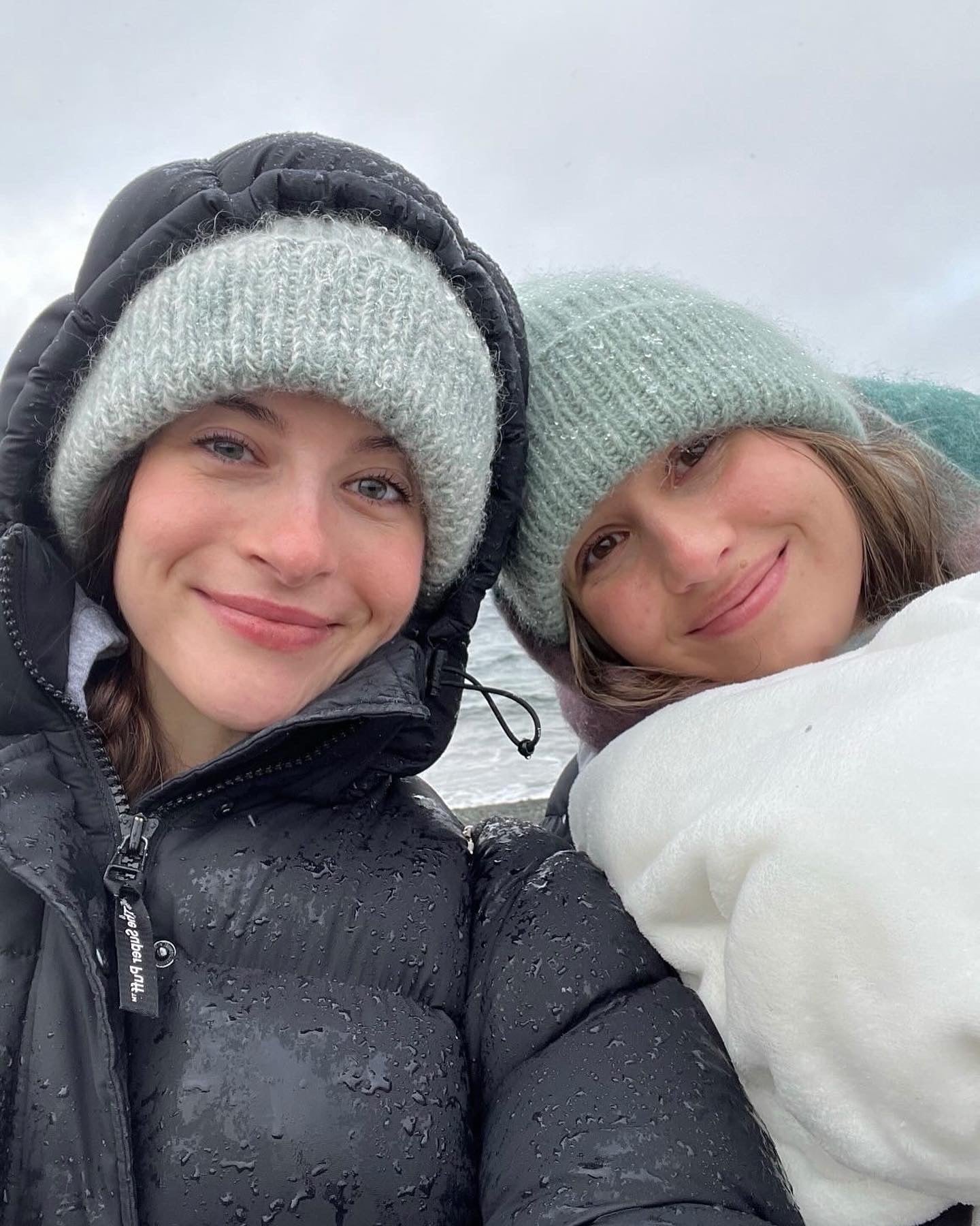 Two girls smiling and wearing the hand-knitted wooly tops hat in blue and green.