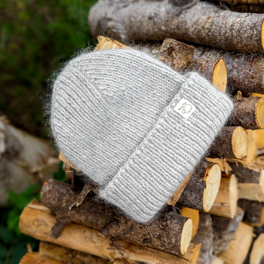 Hand-knitted Wooly Top hat in grey sitting on a pile of logs.
