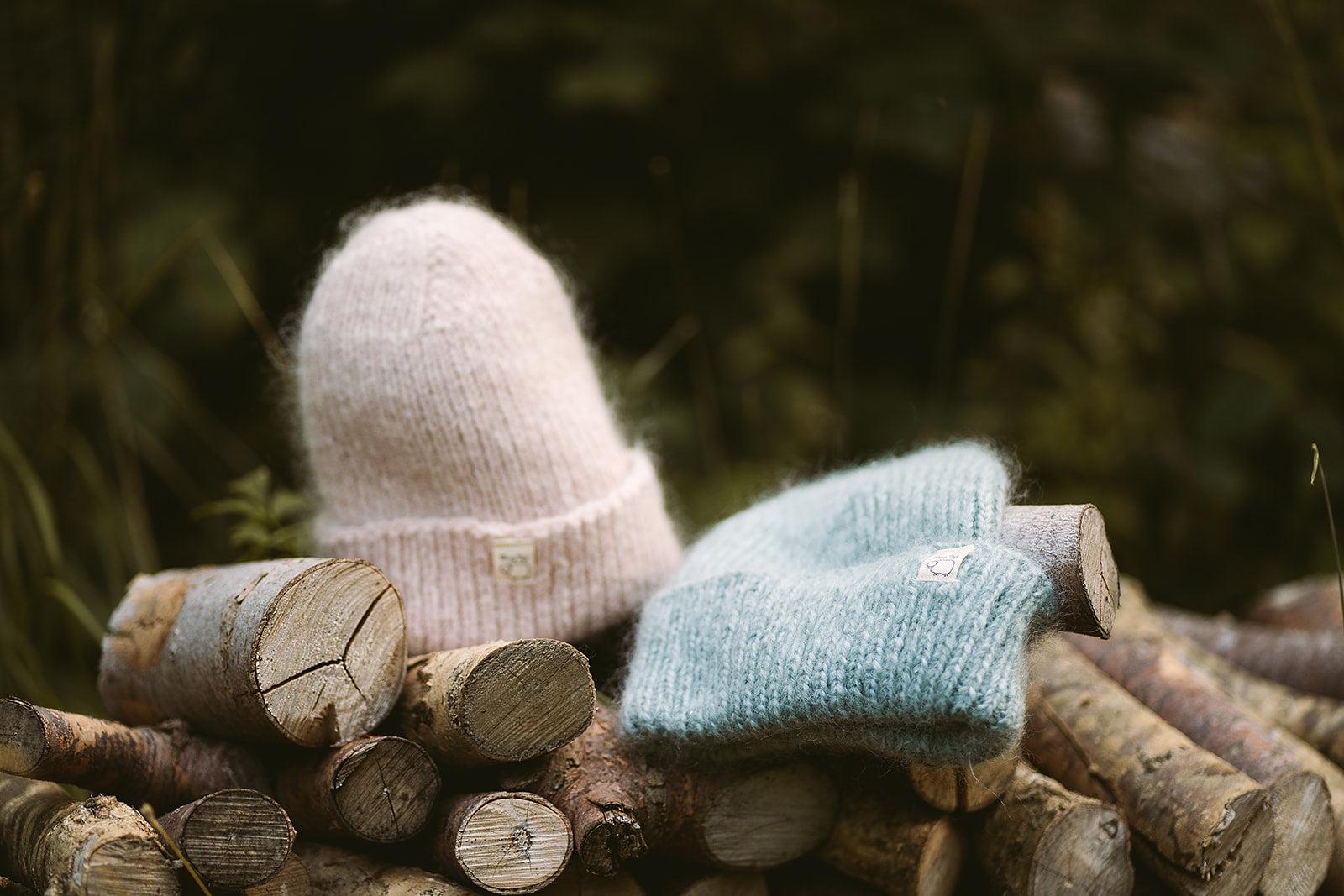 Hand-knitted Wooly Top hats in pink  and blue sitting on a pile of logs.