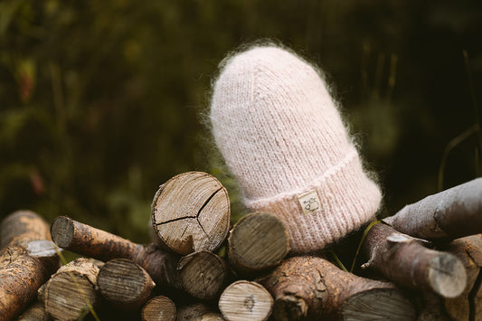 Hand-knitted Wooly Top hat in pink sitting on a pile of logs.