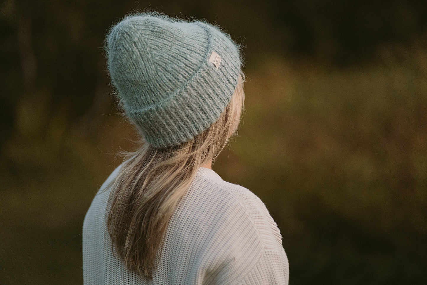 A girl standing back on wearing the hand-knitted wooly top hat in green.